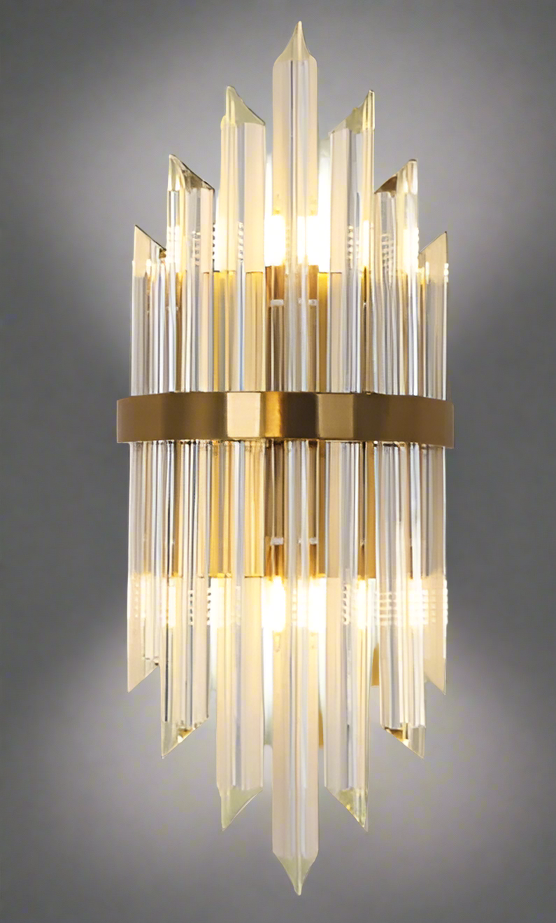 Decorative wall light fixture with clear glass panels and gold metal accents on a gray background